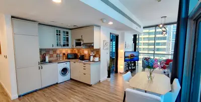 a kitchen with white cabinets and a table with flowers on it at La Buena Vida Holiday Homes - Luxe 1BD, boutique apt full lakeview 1m to Metro, Lake & Almas Tower in Dubai