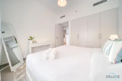a white bedroom with a large white bed and a mirror at Graceful 1BR at Park Heights Dubai Hills MBR City by Deluxe Holiday Homes in Dubai