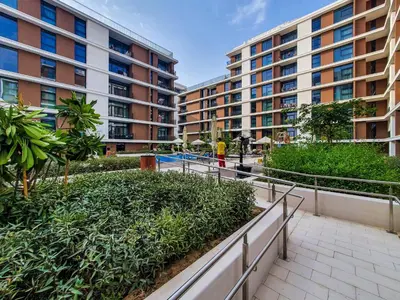 a person walking down a walkway in front of buildings at Brand new 1 bedroom apartment Dubai Hills 601 in Dubai