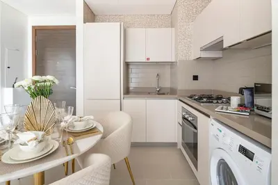 a white kitchen with a table and chairs and a dishwasher at Frank Porter - Sobha Creek Tower B in Dubai