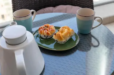 a table with a plate of cupcakes and two coffee cups at Vacay Lettings - 2BHK with Dubai Marina View in Dubai