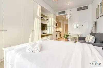a white bedroom with a white bed with two white towels at Cheerful Studio at Belgravia Tower JVC by Deluxe Holiday homes in Dubai