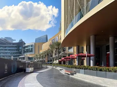 a street in a shopping center with palm trees and buildings at Trophy - Downtown Scape Views Suite in Dubai