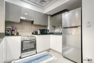 a kitchen with white cabinets and a stainless steel refrigerator at Refined 1BR at Bella Rose Barsha South by Deluxe Holiday Homes in Dubai