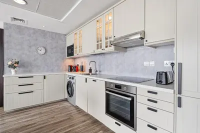 a kitchen with white cabinets and a sink and a dishwasher at Modern & Spacious 2-Bed Condo with Panoramic Lake Views, Dual Balconies, Steps from Dubai JLT Metro By 