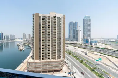 a tall building next to a river in a city at GlobalStay Business Bay Waves Tower Apartments Dubai in Dubai