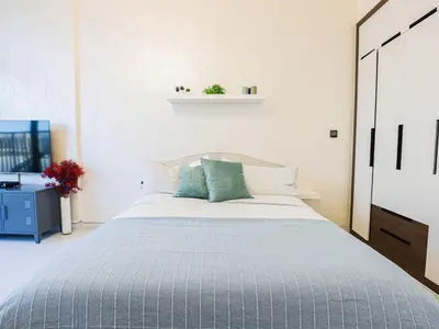 a white bedroom with a large bed with blue pillows at Elite LUX Holiday Homes - Modern Style Studio Superior Facilities in Arjan Dubai in Dubai