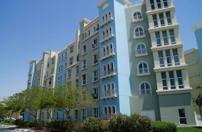 a tall blue building with white windows and trees at Discovery Gardens Haven Studios in Dubai