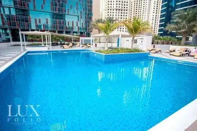 a large blue pool with palm trees and buildings at Beach apartment in Dubai in Dubai