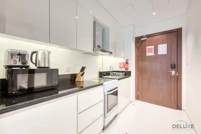 a kitchen with white cabinets and a wooden door at Luxuriant Studio at Golf Promenade 2A DAMAC Hills by Deluxe Holiday Homes in Dubai
