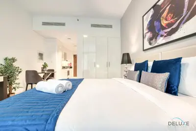 a bedroom with a large white bed with blue pillows at Luxuriant Studio at Golf Promenade 2A DAMAC Hills by Deluxe Holiday Homes in Dubai