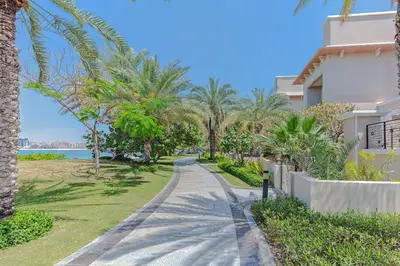 a walkway in front of a house with palm trees at Fully-equppied studio with private beach and pool in Dubai