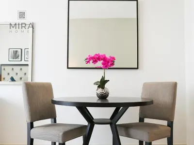 a table with two chairs and a vase with a pink flower at Mira Holiday Homes - Newly serviced apartment in Dubai South in Dubai