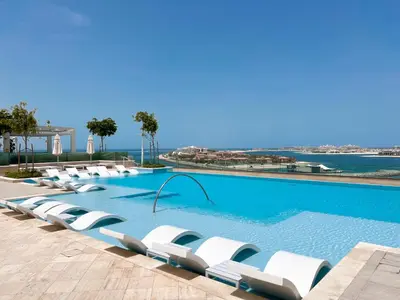 a row of white lounge chairs in a swimming pool at Beachfront 2BR with Spectacular Sea and Palm Views - 17AB06 in Dubai