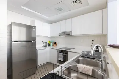 a kitchen with white cabinets and a stainless steel refrigerator at Palmar One Bedroom with Private Beach! in Dubai