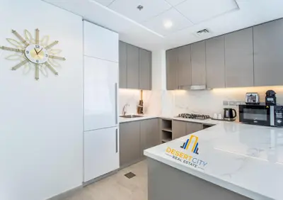 a kitchen with white cabinets and a clock on the wall at 2 Bed in Azzizi Farhad with Burj Khalifa view by Desert City Stays in Dubai