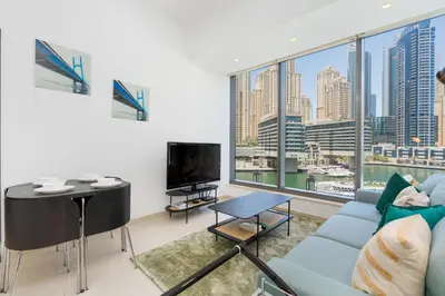 a living room with a blue couch and a large window at Vacay Lettings - Silverene Marina Retreat - Waterfront Apartment Steps from Marina Mall in Dubai