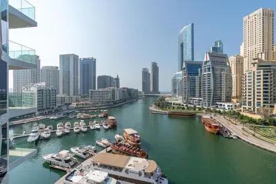 a river with boats docked in a city with tall buildings at Vacay Lettings - Waterfront Luxury home with full Marina view in Dubai