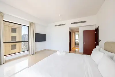 a white bedroom with a couch and a large window at Deluxe Retreat In JBR - Million Dollar View - Balcony in Dubai