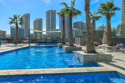 a swimming pool with palm trees and a city skyline at Modern 1BR in Dubai Marina Near Metro & Beach in Dubai