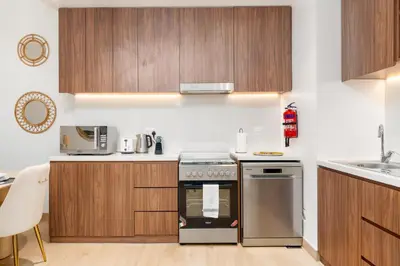 a kitchen with wooden cabinets and a stove top oven at Stylish 1BR Apartment in La Mer Dubai with Balcony and Partial Marina Views in Dubai