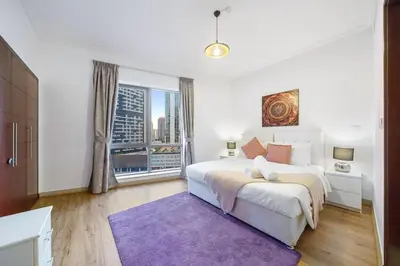 a white bedroom with a large bed and a purple rug at Contemporary & Roomy 2BR with Burj Khalifa view in Dubai