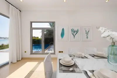 a white dining room with a table and a large window at Maison Privee - Exclusive Villa with Private Pool, Garden & Beach in Dubai