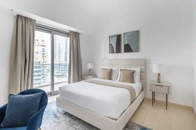 a white bedroom with a bed and a blue chair at Frank Porter - The Jwls T2 in Dubai