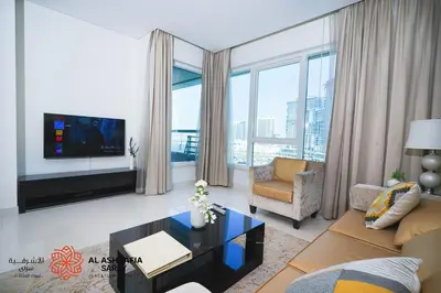 a living room with a couch and a tv and some windows at Al Ashrafia Saray Marvelous 1 BR - Damac Maison - Canal View in Dubai