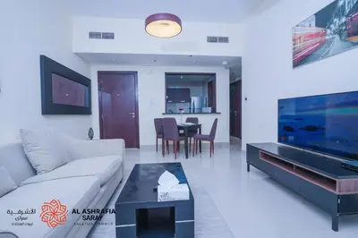 a living room with a couch and a tv and a table at Alasharafia Saray, Spacious 1BR apartment in Sport City in Dubai