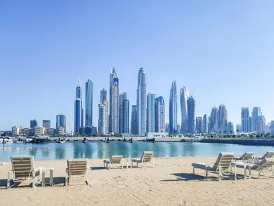 a group of chairs on the beach in front of a city at Maison Privee - Deluxe 3BR Apt with Dubai Marina Vws & Beach Access in Dubai