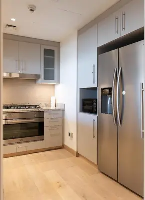 a kitchen with white cabinets and a stainless steel refrigerator at EDEN'S Homes & Villas - Boulevard Point in Dubai