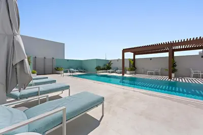 a swimming pool with blue chaise lounge chairs next to a building at Silkhaus cozy studio in JVC Luma21 in Dubai