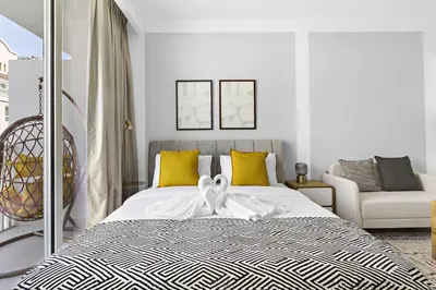 a white bedroom with a bed with yellow pillows at Silkhaus cozy studio in JVC Luma21 in Dubai