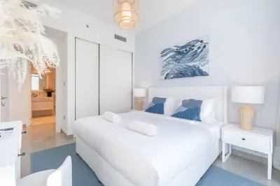 a white bedroom with a large white bed and a lamp at Vogue Emaar Beachfront Beach Vista near JBR and Palm Jumeirah, One Bedroom Apartment with Balcony and Private Beach, Access to all Amenities in Dubai