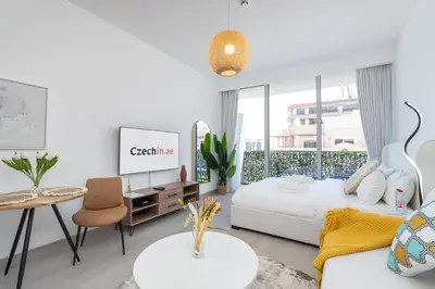 a white living room with a white bed and a table at Brand New & Modern Studio in JVC in Dubai