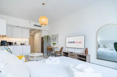 a white living room with a bed and a kitchen at Brand New & Modern Studio in JVC in Dubai