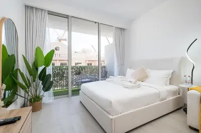 a white bedroom with a bed and a large window at Brand New Vibrant Studio in JVC in Dubai