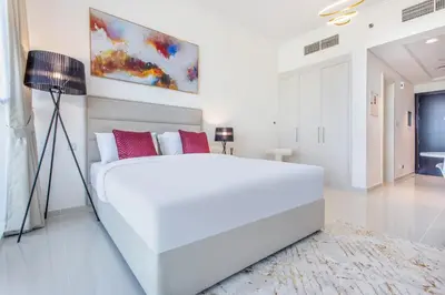 a white bedroom with a large bed and a lamp at Full Golf View Studio in Damac Hills - Host & Stay in Dubai