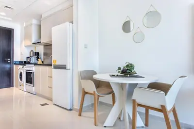 a white kitchen with a white table and chairs at Full Golf View Studio in Damac Hills - Host & Stay in Dubai