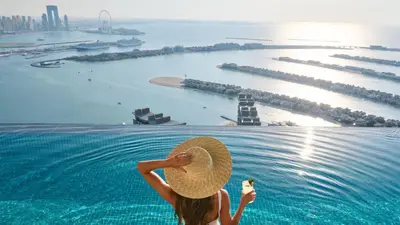 a woman in a straw hat is looking at the water at LHG PALM JUMEIRAH Tallest RoofTop Pool in Dubai