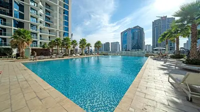 a large swimming pool with palm trees and buildings at Bright Deluxe Studio canal view - Special offer in Dubai