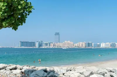 a beach with people in the water with a city in the background at Seaside Serenity: 1-BR Apartment with Beach Access in Dubai